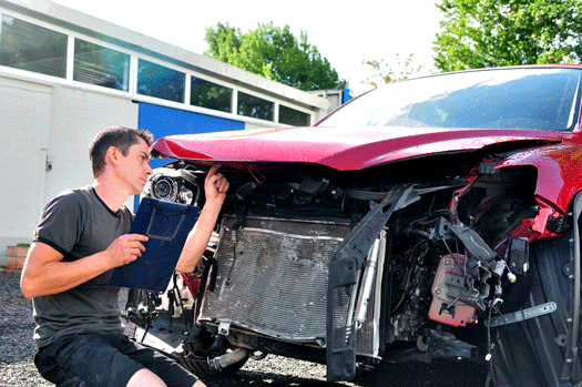 Photos a wrecked car with the hood up and a man inspecting it.